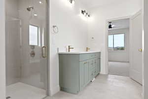 Bathroom with ceiling fan, a shower stall, tile patterned flooring, a sink, and double vanity