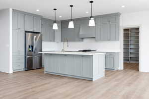 Kitchen featuring stainless steel fridge with ice dispenser, a sink, light countertops, light wood-style floors, and custom range hood