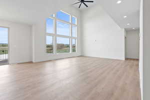 Unfurnished living room featuring ceiling fan, light wood-style flooring, recessed lighting, a high ceiling, and baseboards