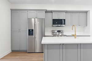 Kitchen with light wood-style flooring, gray cabinets, appliances with stainless steel finishes, light stone counters, and baseboards