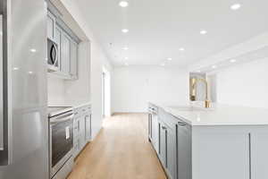 Kitchen with a sink, recessed lighting, stainless steel appliances, gray cabinets, and light wood-style flooring