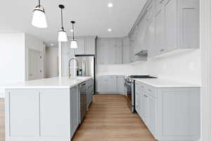 Kitchen with light wood-style flooring, recessed lighting, a kitchen island with sink, stainless steel appliances, and gray cabinetry