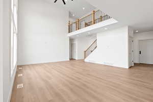 Unfurnished living room with light wood finished floors, recessed lighting, visible vents, and stairs