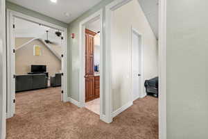 Hallway with baseboards, light colored carpet, and vaulted ceiling