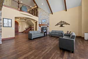 Living area with a stone fireplace, stairway, dark wood-style floors, high vaulted ceiling, and arched walkways