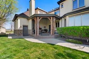Rear view of house with a patio area, stucco siding, stone siding, and a lawn
