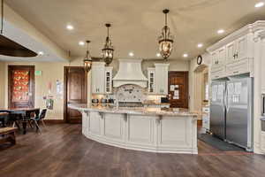 Kitchen with baseboards, freestanding refrigerator, premium range hood, and dark wood finished floors