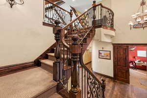 Stairs with wood finished floors, a notable chandelier, baseboards, and a towering ceiling
