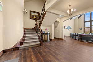 Foyer entrance featuring arched walkways, an inviting chandelier, stairs, and wood finished floors