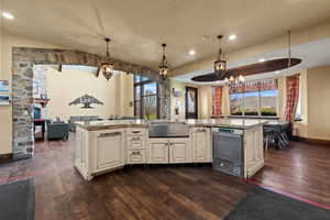 Kitchen featuring light stone countertops, a wealth of natural light, dark wood-style flooring, a sink, and a notable chandelier