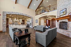 Living area with a stone fireplace, dark wood-type flooring, beamed ceiling, high vaulted ceiling, and arched walkways