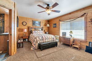 Bedroom with wood walls, ceiling fan, and carpet floors