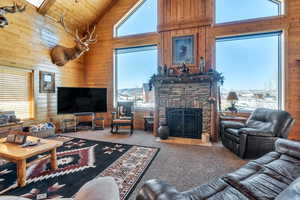 Carpeted living area with high vaulted ceiling, wood walls, a stone fireplace, and a wealth of natural light