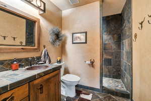 Full bath featuring visible vents, baseboards, toilet, vanity, and tiled shower