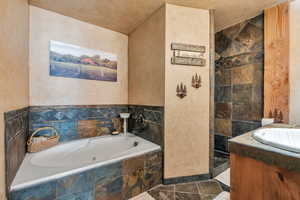 Bathroom with a whirlpool tub, stone finish floor, vanity, and a textured wall