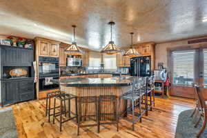 Kitchen featuring a sink, light wood-type flooring, a kitchen bar, black appliances, and a large island with sink