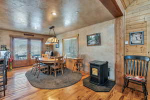 Dining room featuring a textured wall, a wood stove, wood finished floors, and a healthy amount of sunlight