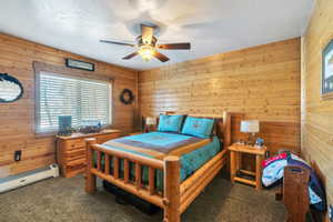 Carpeted bedroom featuring wooden walls, a baseboard radiator, and a ceiling fan