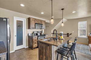 Kitchen featuring a textured ceiling, a center island with sink, a breakfast bar area, stainless steel appliances, and a sink