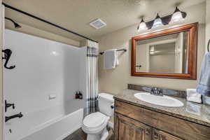 Bathroom featuring visible vents, toilet, shower / tub combo with curtain, a textured ceiling, and vanity