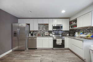 Kitchen with open shelves, a sink, white cabinetry, stainless steel appliances, and backsplash
