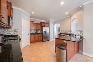 Kitchen with arched walkways, a peninsula, stainless steel refrigerator with ice dispenser, a sink, and backsplash
