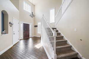 Foyer entrance with a towering ceiling, stairway, baseboards, dark wood-style floors, and a notable chandelier