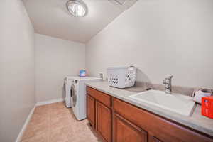 Clothes washing area featuring baseboards, a sink, light tile patterned floors, cabinet space, and washing machine and clothes dryer