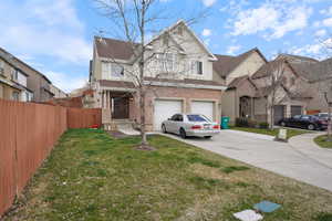 Traditional-style house with concrete driveway, an attached garage, a front yard, brick siding, and fence
