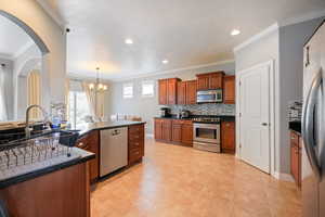 Kitchen with ornamental molding, dark countertops, a chandelier, stainless steel appliances, and decorative backsplash