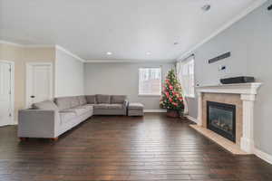 Living room featuring baseboards, ornamental molding, recessed lighting, a tiled fireplace, and dark wood-style floors