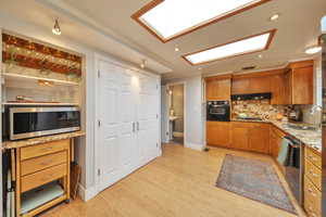 Kitchen with appliances with stainless steel finishes, under cabinet range hood, brown cabinetry, a skylight, and a sink