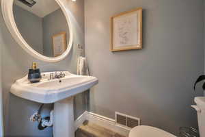 Bathroom featuring toilet, wood finished floors, baseboards, and visible vents