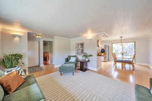 Living area featuring a chandelier, light wood-style floors, baseboards, and crown molding
