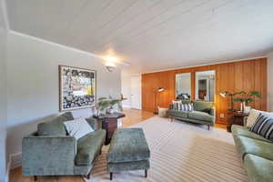 Living area featuring crown molding, wood finished floors, wooden walls, and visible vents