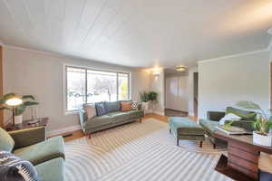 Living room featuring crown molding, wood finished floors, baseboards, and visible vents