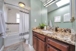 Full bath with toilet, wood finished floors, vanity, and shower / bathtub combination with curtain