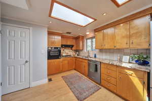 Kitchen featuring a sink, ornamental molding, under cabinet range hood, stainless steel appliances, and a skylight