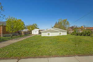 Exterior space featuring a detached garage, concrete driveway, a lawn, fence, and an outbuilding