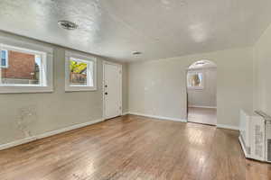 Interior space with hardwood / wood-style flooring, arched walkways, heating unit, and visible vents