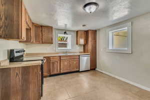 Kitchen with stainless steel appliances, light countertops, baseboards, and brown cabinetry