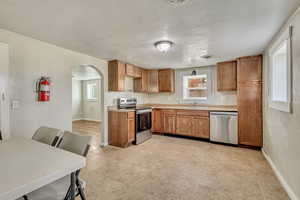 Kitchen with a sink, brown cabinetry, arched walkways, stainless steel appliances, and light countertops