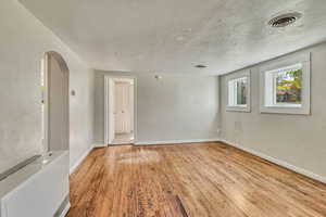 Unfurnished room with arched walkways, wood finished floors, visible vents, and baseboards