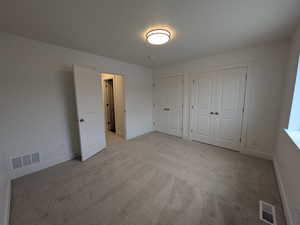 Unfurnished bedroom with visible vents, light colored carpet, two closets, and baseboards