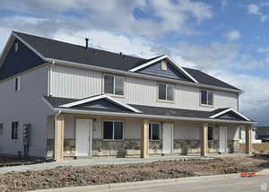 View of front of home featuring a porch, a shingled roof, and stone siding