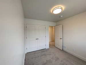 Unfurnished bedroom with a closet, baseboards, carpet flooring, a textured ceiling, and visible vents