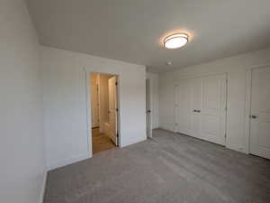 Unfurnished bedroom featuring ensuite bathroom, baseboards, and carpet floors