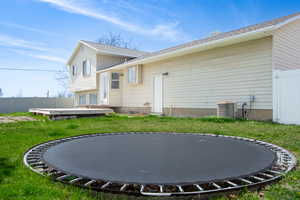 Rear view of house featuring a trampoline, cooling unit, fence, and a lawn