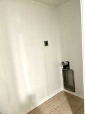Clothes washing area featuring hookup for an electric dryer, light tile patterned floors, laundry area, and baseboards