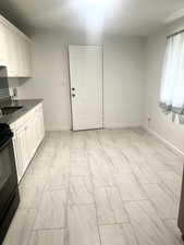 Kitchen with marble finish floor, black electric range, baseboards, and white cabinetry